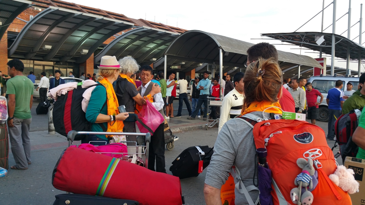 Großer Trubel am Flughafen und Begrüßung durch/von Kaji, der uns abgeholt hat. Auf dem orangen Begrüßungsschal (Khata, Khatag) sind die nepalesischen Glückssymbole zu erkennen. Der Schal ist ein Symbol für das reine Herz des Überreichenden. Er steht für Glück, Wohlwollen und Mitgefühl. 
