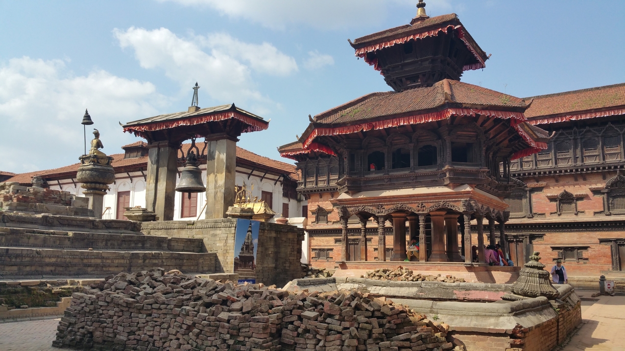 König Bhupatindra Malla sitzt auf der Säule vor dem goldenen Tor des Königspalasts. Daneben die Taleju Glocke und den achteckigen Cyasilim Mandir.
